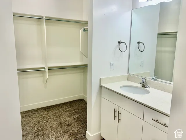 Vanity featuring a stone-composite countertop, undermount sink, brushed nickel hardware, and full-width mirror, paired with a walk-in closet containing built-in shelving and closet rods