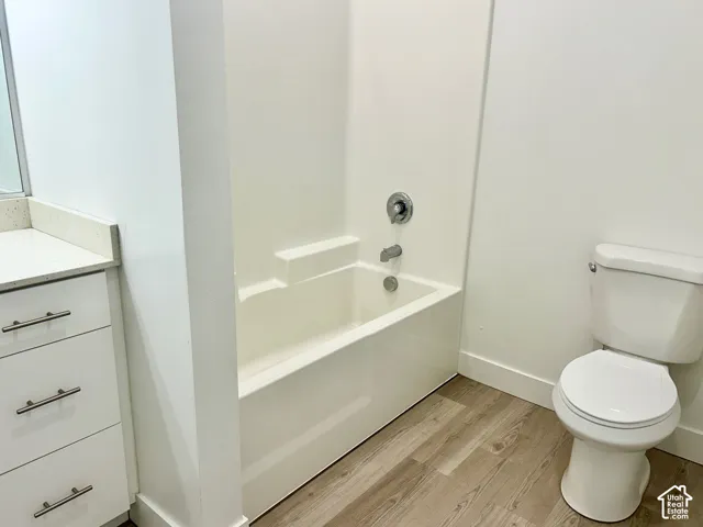 Bathroom featuring a composite tub and shower surround, white vanity with stone-finish countertop, brushed metal hardware, and wood-finish flooring