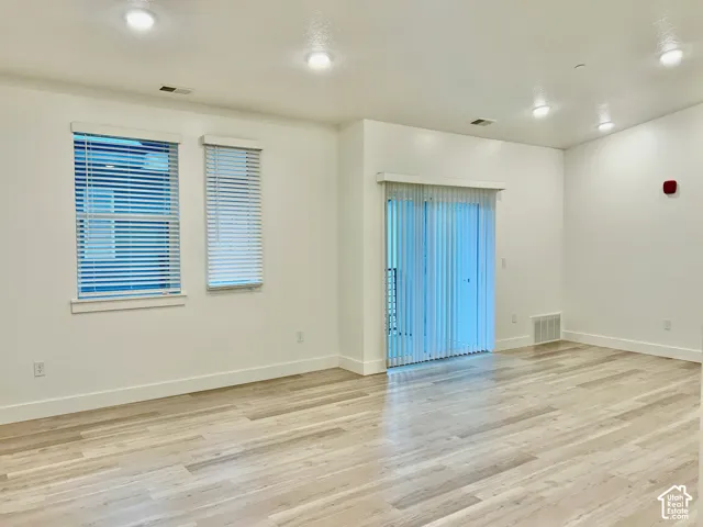 Open interior space featuring light-toned wood-finish flooring, recessed ceiling lighting, sliding glass doors with vertical blinds, and dual windows with horizontal blinds
