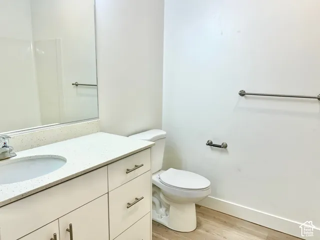 Bathroom featuring a vanity with light-toned solid surface countertop and undermount sink, large wall-mounted mirror, metal hardware, and wood-finish flooring