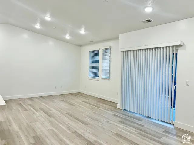 Interior space featuring vaulted ceilings, wood-finish flooring, recessed lighting, double-pane windows, and vertical blinds on the sliding glass door