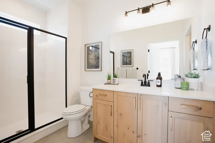 Bathroom featuring a light wood vanity with white countertop, integrated sink with matte black faucet, walk-in shower with matte black frame, and wall-mounted vanity lighting