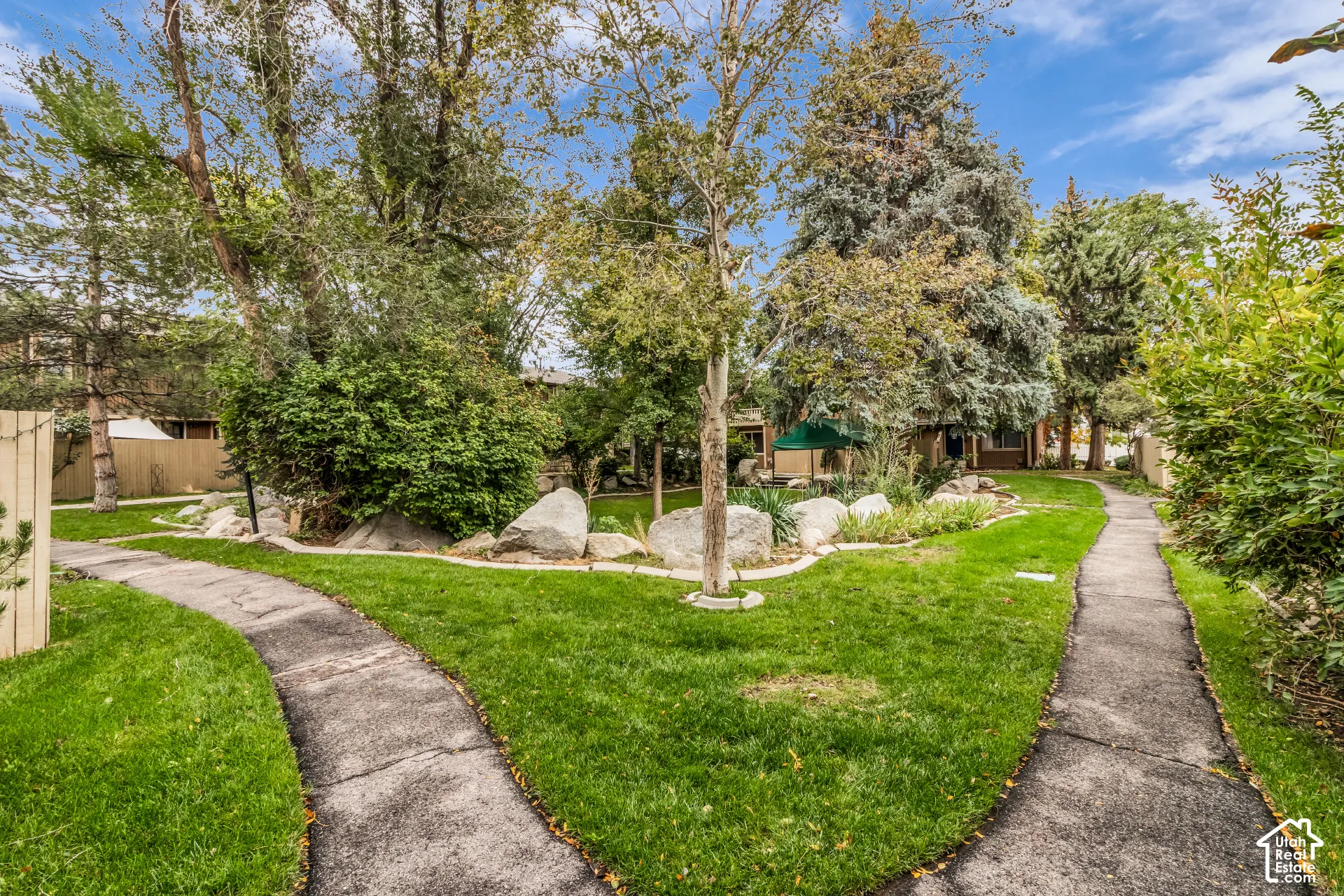 Expansive grounds featuring paved walking paths, manicured lawn, mature trees, and natural rock landscaping