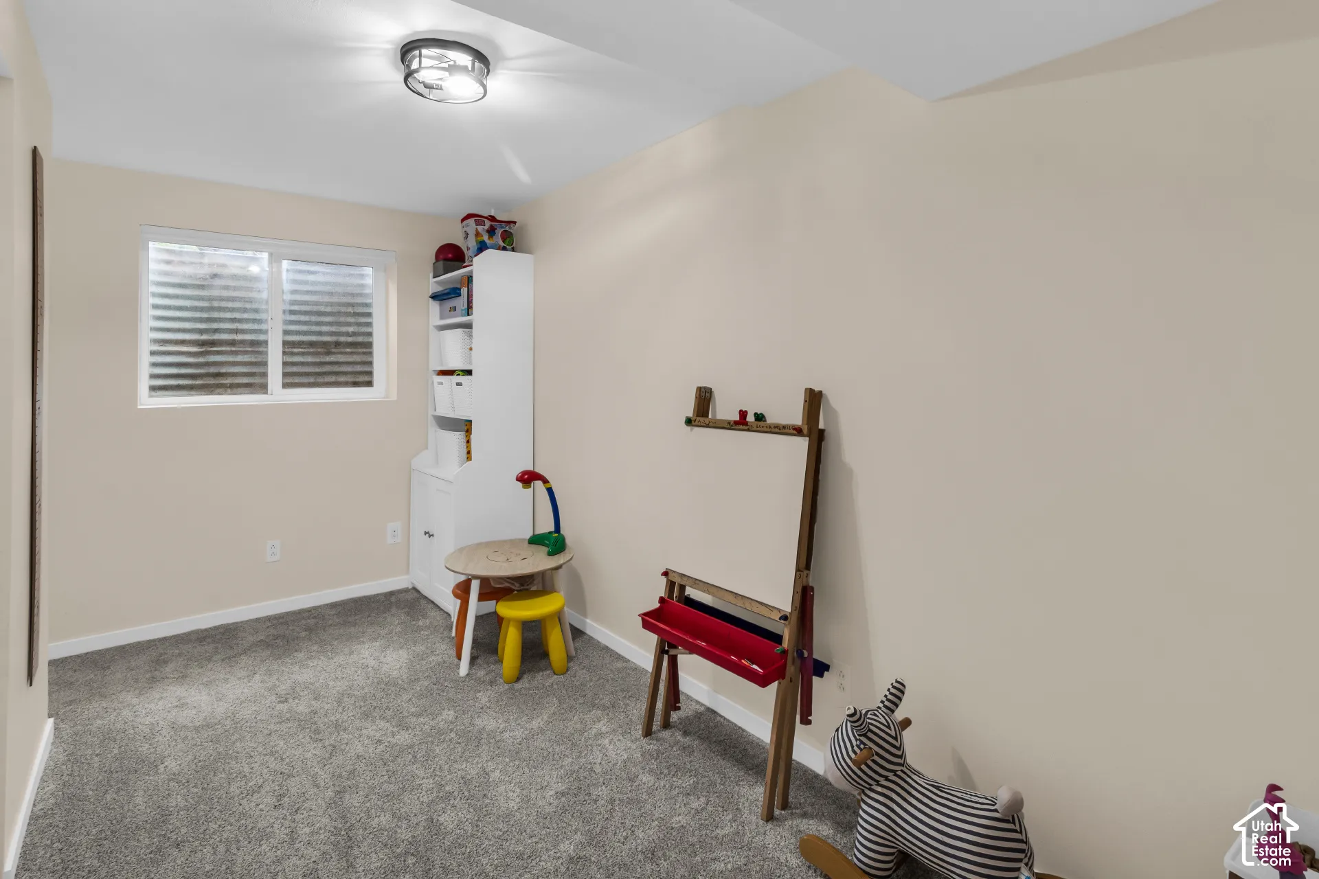 Neutral-toned interior space featuring carpeting, a built-in cabinet, a single horizontal window, and a flush-mount ceiling light fixture
