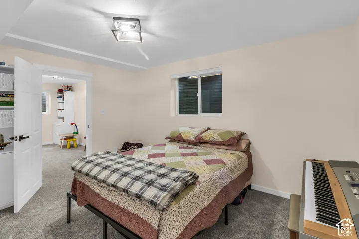 Neutral interior space featuring gray wall-to-wall carpeting, a rectangular window with a window well, and a square-profile ceiling-mounted light fixture with a black frame