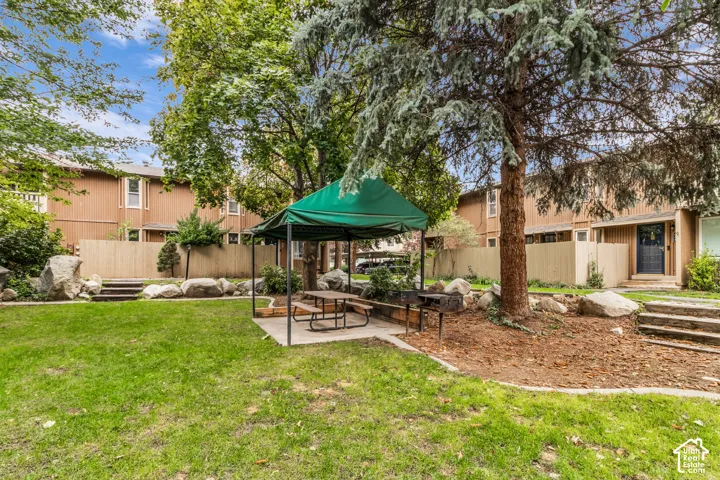 Common area featuring a manicured lawn, mature trees, tiered stone retaining walls, and concrete step accents