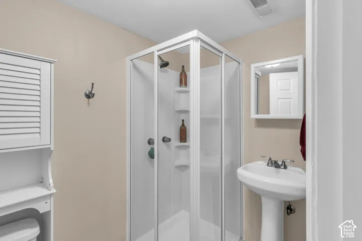 Corner shower enclosure with sliding glass doors, pedestal sink with dual-handle faucet, wall-mounted medicine cabinet, and white built-in storage unit