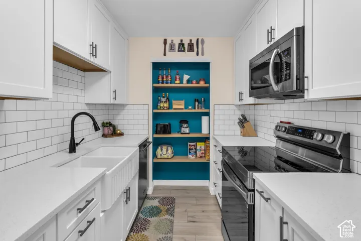 Kitchen featuring white shaker-style cabinetry, quartz countertops, white subway tile backsplash, a farmhouse-style apron sink with a matte black faucet, and built-in shelving