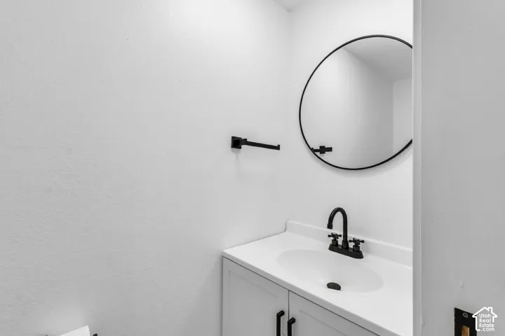 Vanity with a white integrated countertop and basin, matte black faucet, shaker-style base cabinetry, circular mirror with a matte black frame, and matching matte black wall-mounted towel ring