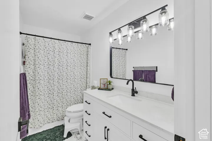 Bathroom featuring a white vanity with matte black hardware, stone-surface countertop, rectangular undermount sink, and a rectangular mirror with integrated multi-light fixture