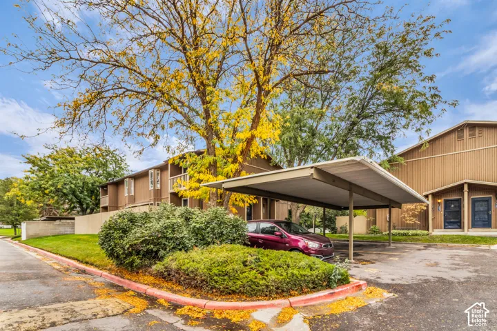 Covered carport, multi-level building with wood-tone siding, asphalt paving, and mature landscaping