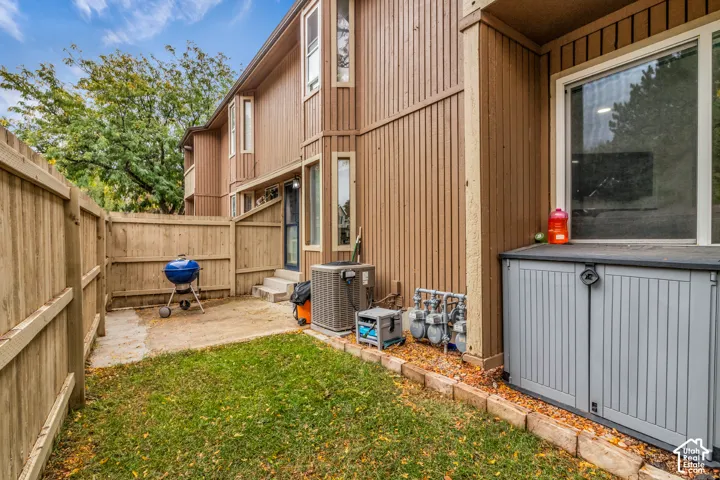 Vertical wood-siding exterior with a fenced yard, concrete patio, and mature trees