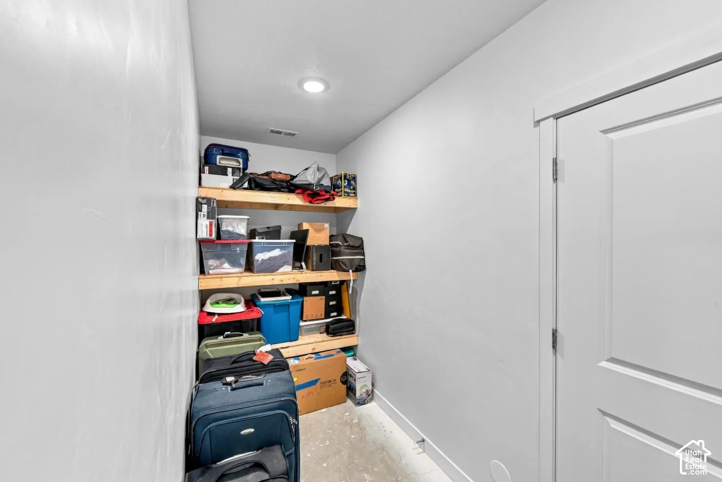 Storage area featuring three tiers of built-in wooden shelving and recessed ceiling lighting