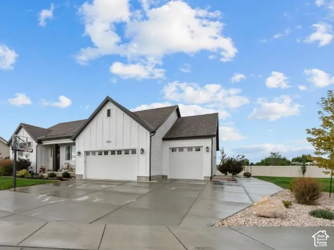 Single-story residence featuring white board-and-batten siding, a multi-gabled roofline, an attached three-car garage, and an expansive concrete driveway