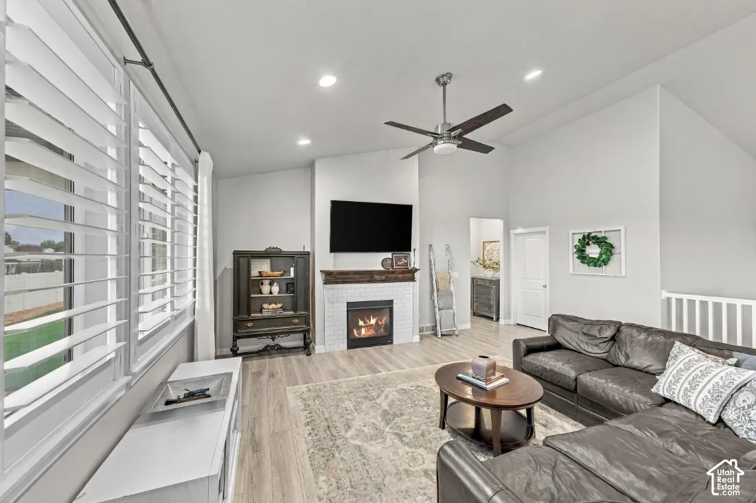 Living area featuring vaulted ceilings, wood-finish flooring, white brick fireplace with a timber mantel, recessed lighting, and plantation shutters