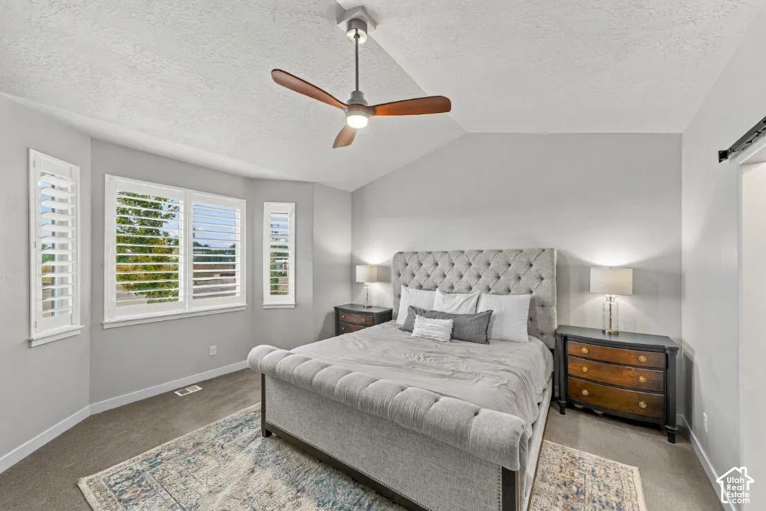 Vaulted ceiling with a centrally mounted three-blade fan, large multi-pane windows, and white plantation shutters