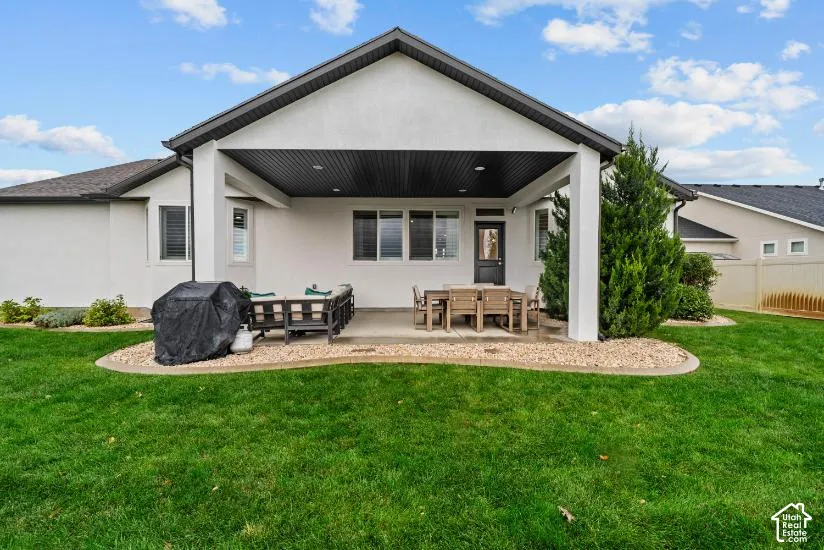 Covered concrete patio featuring recessed lighting, stucco exterior, peaked roofline, and landscaped rock edging surrounding a grass lawn