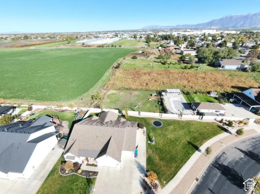 Aerial perspective of a multi-gabled residence featuring a concrete driveway, an expansive lawn, a privacy-fenced rear perimeter, and a mountain range backdrop