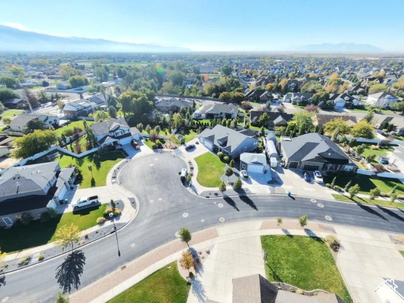 Aerial perspective of a residential cul-de-sac featuring paved driveways, manicured lawns, asphalt roadways, and mountain backdrop