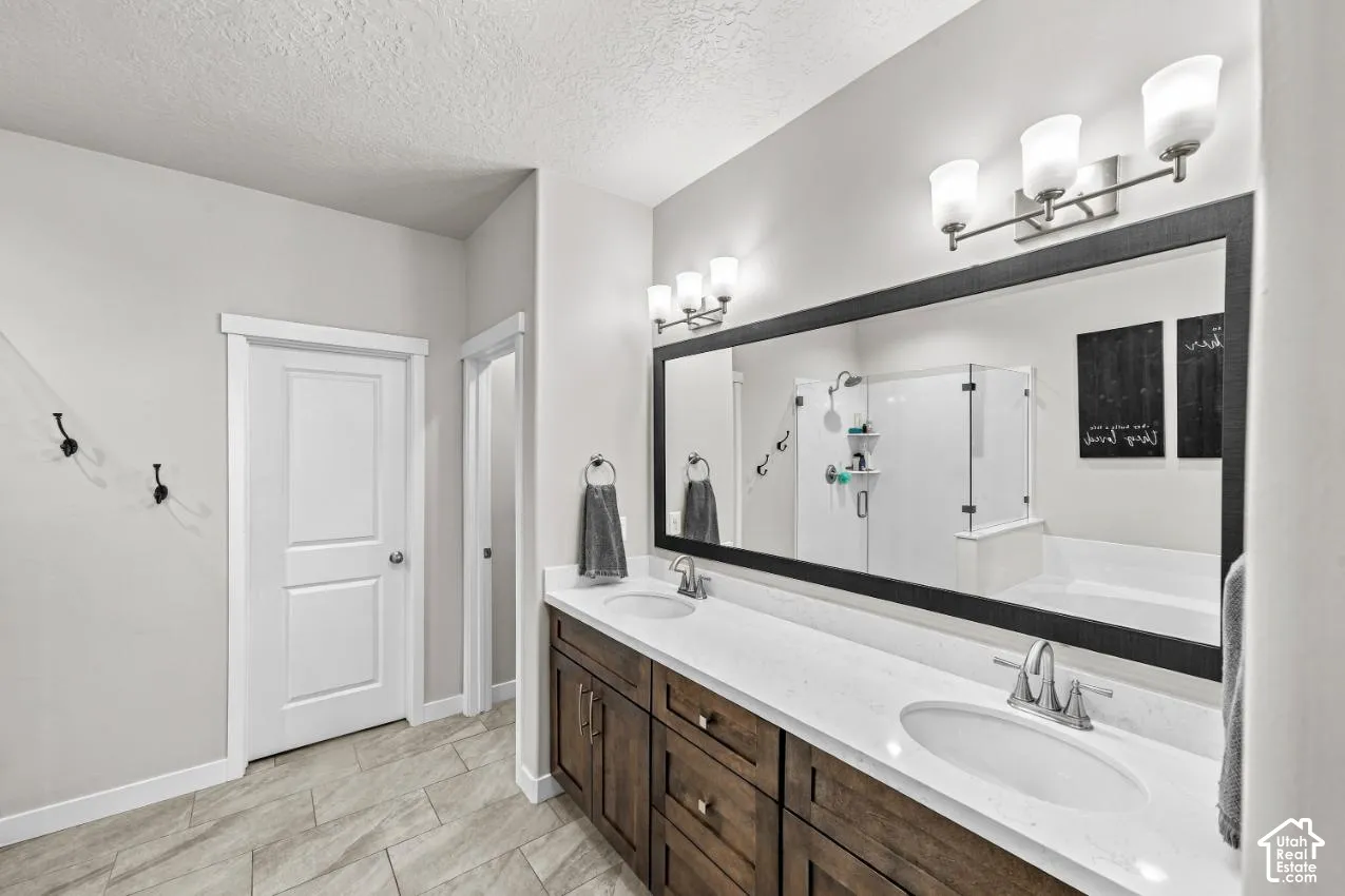 Double vanity with a light-toned countertop, under-mount sinks, dark-toned cabinetry, and a large framed mirror with dual wall-mounted light fixtures