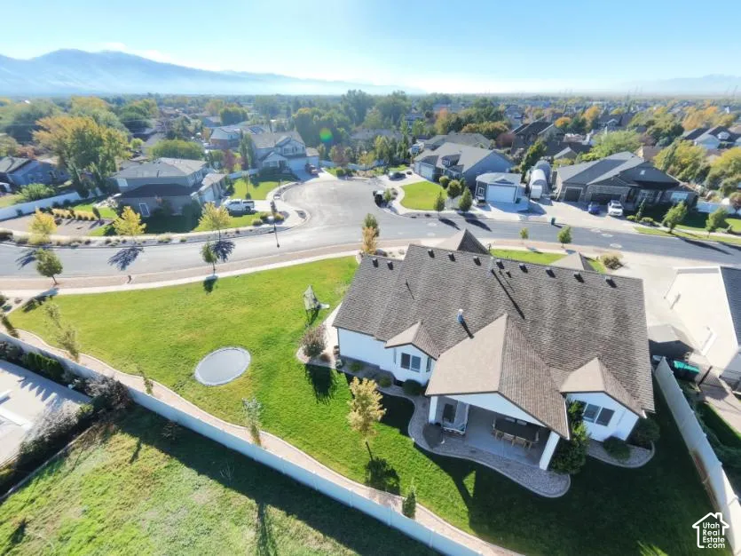 Aerial view of a residential property featuring a large fenced yard, a covered concrete patio, a manicured lawn, and expansive mountain scenery