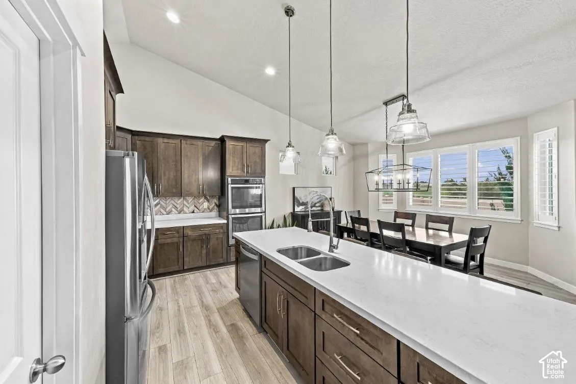 Kitchen featuring vaulted ceilings, wood-finish cabinetry, quartz countertops, a herringbone-patterned tile backsplash, and stainless steel built-in appliances