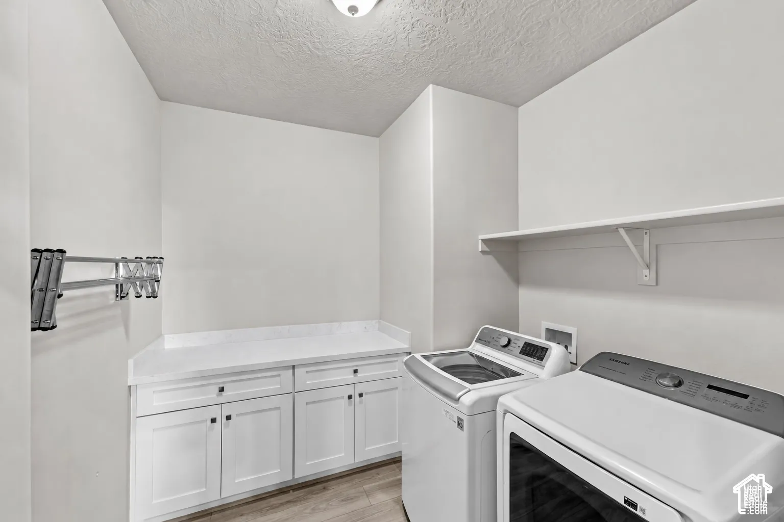 Dedicated laundry area featuring white shaker-style cabinetry, solid-surface countertop, mounted drying rack, and open shelving