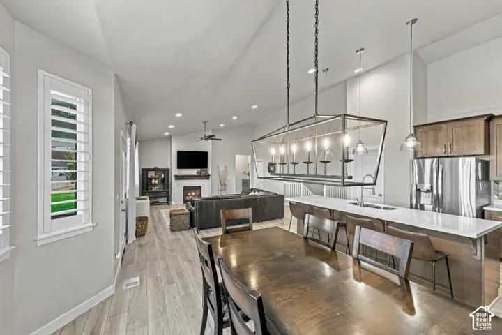 Vaulted ceilings, kitchen island with quartz countertop, rectangular iron pendant lighting, fireplace with mantel, and wood-finish flooring