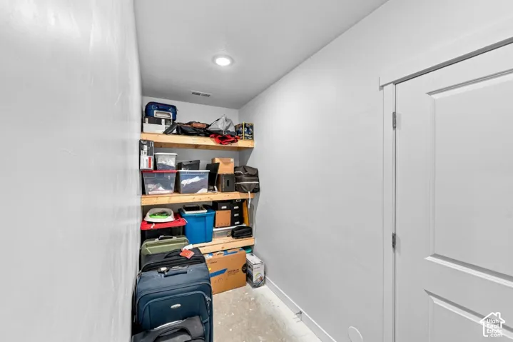 Storage area featuring three tiers of built-in wooden shelving and recessed ceiling lighting