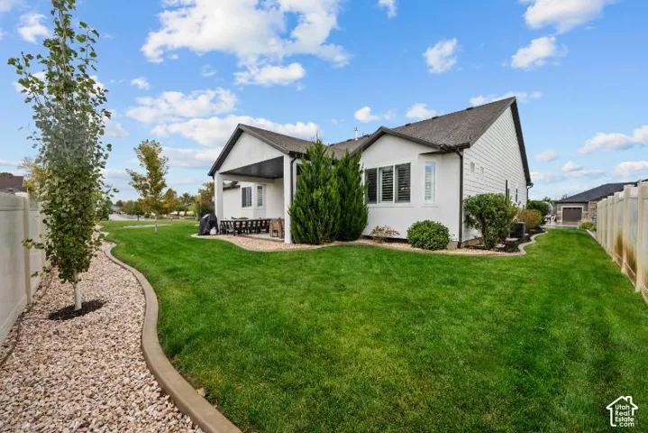 Backyard featuring a covered patio, manicured lawn, concrete curbing, decorative rock borders, and vinyl fencing