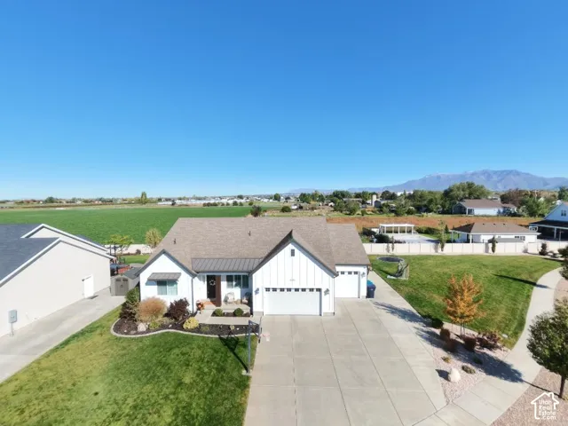 Single-story residence featuring a white vertical-panel exterior, a multi-gabled roof, an attached three-car garage, concrete driveway, and expansive lawn area with mountain background