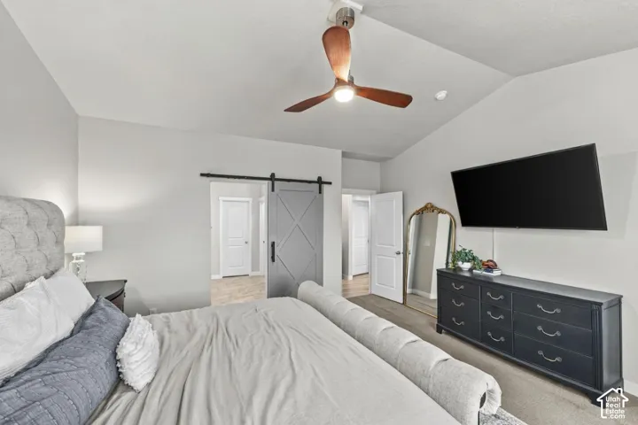 Vaulted ceiling with a three-blade wooden ceiling fan and light fixture, accented by a grey sliding barn door and interior doors with panel detailing