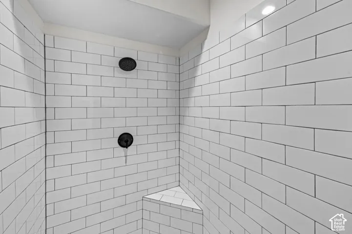 Walk-in shower featuring white subway tile surround, integrated corner bench, and matte black plumbing fixtures