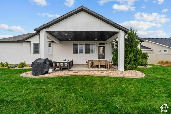 Covered concrete patio featuring recessed lighting, stucco exterior, peaked roofline, and landscaped rock edging surrounding a grass lawn