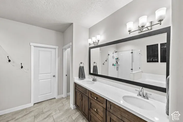 Double vanity with a light-toned countertop, under-mount sinks, dark-toned cabinetry, and a large framed mirror with dual wall-mounted light fixtures