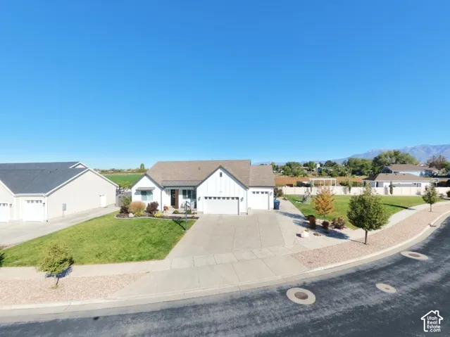 Single-story residence featuring white vertical siding, a front-facing attached three-car garage, expansive manicured lawn, concrete driveway, and mountain backdrop