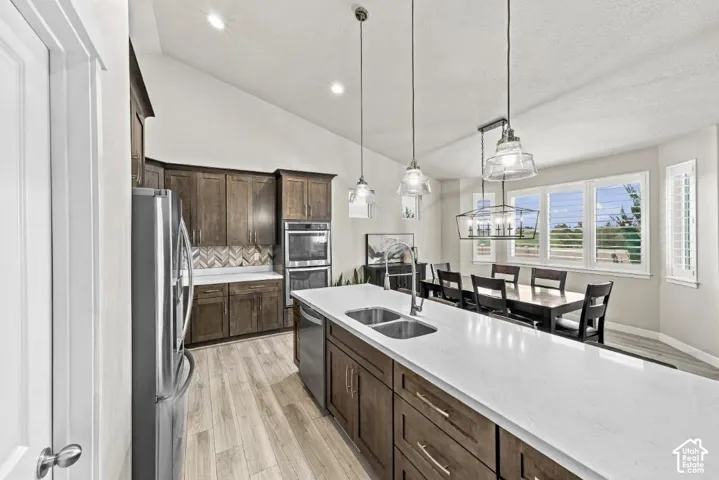 Kitchen featuring vaulted ceilings, wood-finish cabinetry, quartz countertops, a herringbone-patterned tile backsplash, and stainless steel built-in appliances