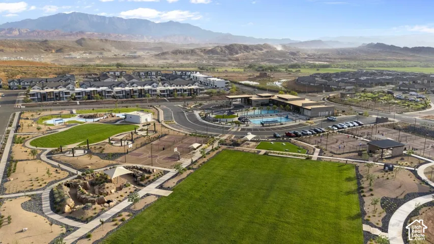 Aerial perspective featuring communal swimming pool, paved sport courts, manicured green space, walking paths, and mountain backdrop