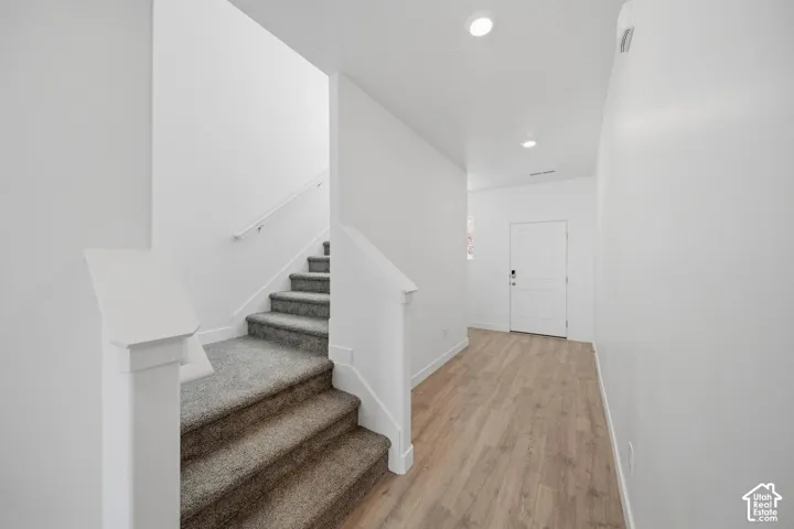 Entryway featuring wood-finish flooring, white panel door, recessed lighting, and carpeted staircase with a white handrail