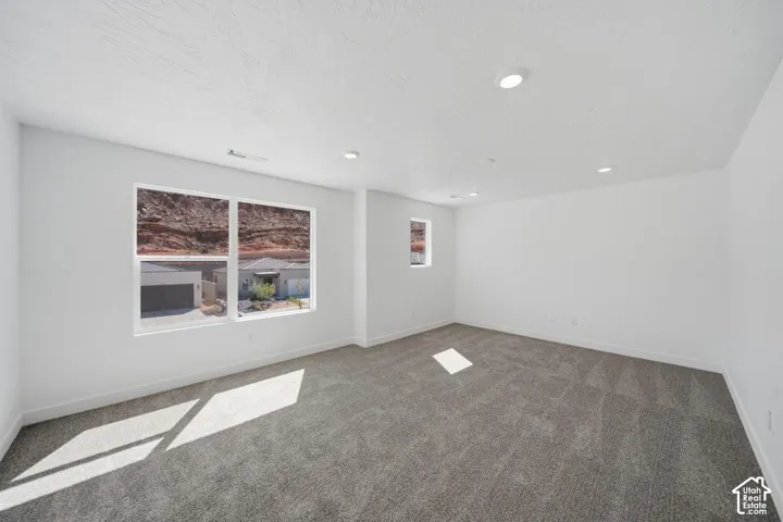 Interior space featuring neutral wall tones, plush wall-to-wall carpeting, recessed ceiling lighting, and windows showcasing a rock formation landscape