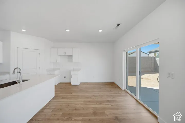 Kitchen featuring a quartz-topped island with an undermount sink, white shaker-style cabinetry, recessed ceiling lighting, wood-finish flooring, and a large sliding glass door