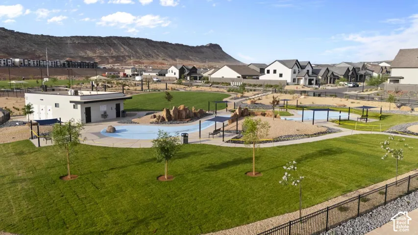 Community park featuring a landscaped lawn, paved walking paths, rock formations, water feature, and mountain backdrop