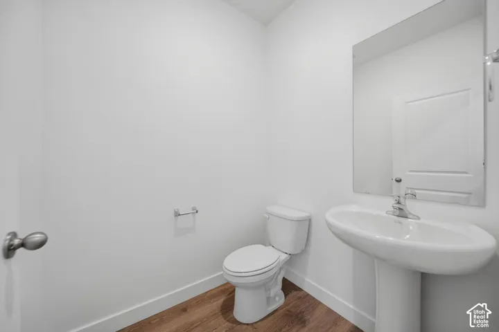 Powder room featuring a pedestal sink, chrome faucet, wall-mounted mirror, and wood-finish flooring