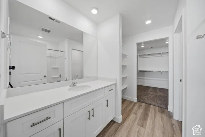 Bathroom featuring a vanity with a solid-surface countertop, white cabinetry, a full-width mirror, recessed lighting, and wood-finish flooring