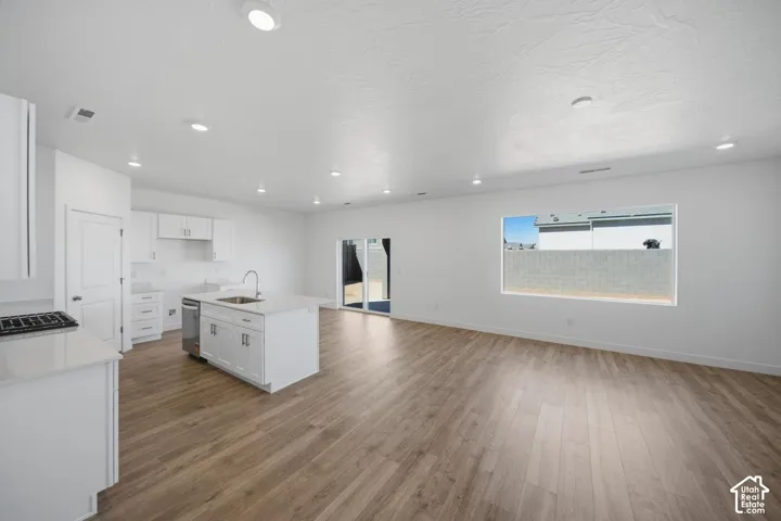 Open floor plan featuring wood-finish flooring, white cabinetry, a center kitchen island with a neutral countertop, recessed lighting, and sliding glass patio doors