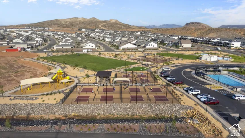 Aerial perspective of community recreation area featuring multiple pickleball courts, a swimming pool, a playground, and expansive green space set against a mountain backdrop