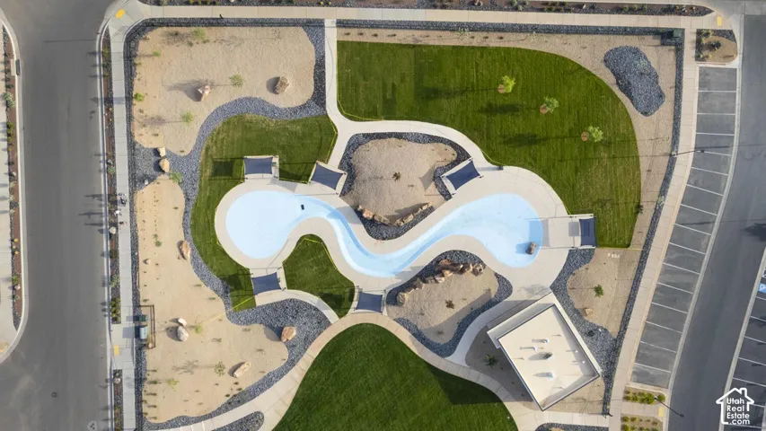 Aerial view of a community recreation area featuring a serpentine-shaped pool, shaded seating structures, manicured lawn, xeriscaped grounds with decorative rock, and paved pathways