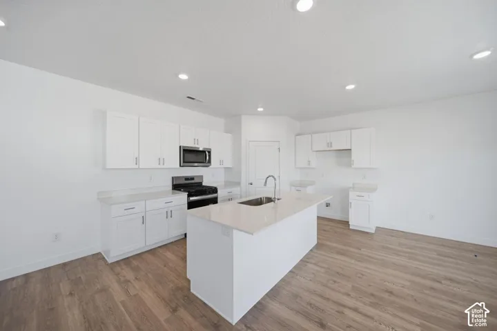 Kitchen featuring white cabinetry, solid-surface countertops, center island with an undermount sink, recessed lighting, and wood-finish flooring
