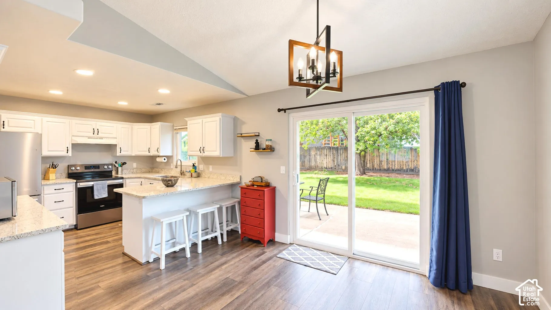 Kitchen featuring white cabinetry, stone-surface countertops, wood-finish flooring, recessed lighting, and a geometric pendant light fixture, with a sliding glass door opening to a rear patio and lawn
