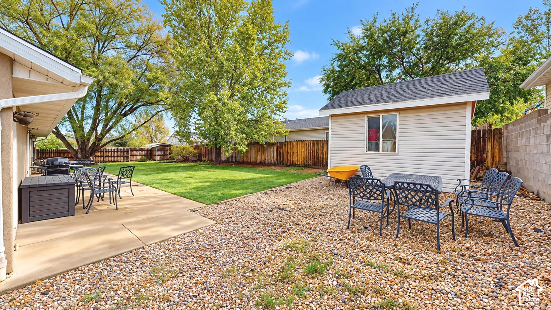 Backyard featuring a concrete patio, gravel hardscaping, detached structure, wood fencing, and mature trees